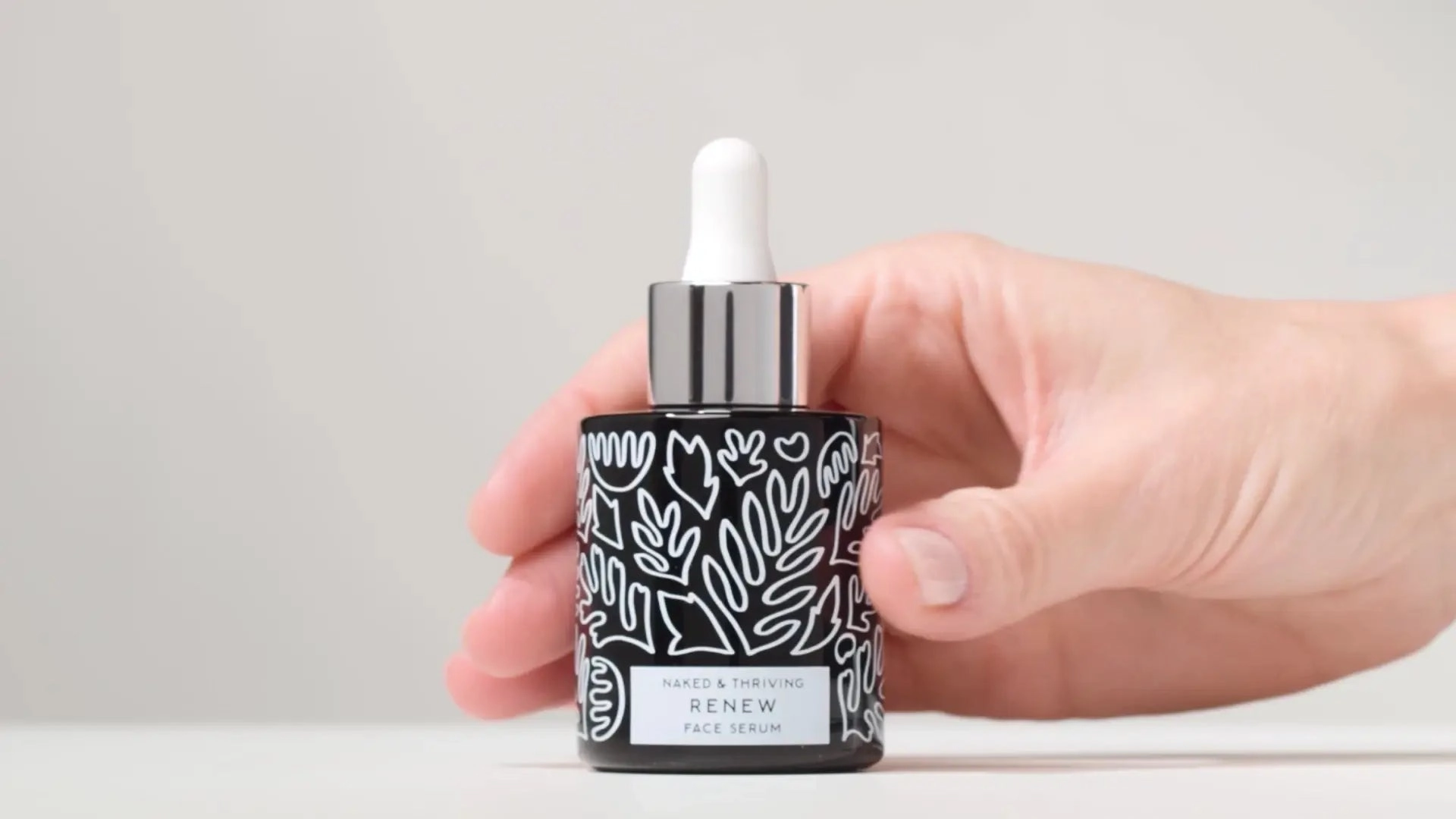 Hand holding a Renew dropper bottle against a soft grey background
